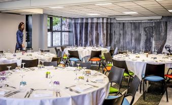 a well - organized dining room with multiple round tables , each set for a meal , and several chairs arranged around them at Ibis Styles Lille Marcq-en-Baroeul