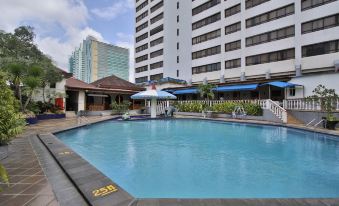 a large outdoor swimming pool surrounded by buildings , with umbrellas and lounge chairs placed around the pool area at Jayakarta Hotel Jakarta