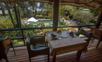 a table with a plate and silverware is set on a wooden deck overlooking a pool and lush greenery at Maravu Taveuni Lodge