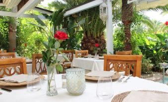 an outdoor dining area with a table set for a meal , surrounded by lush greenery and palm trees at Hotel Simius Playa