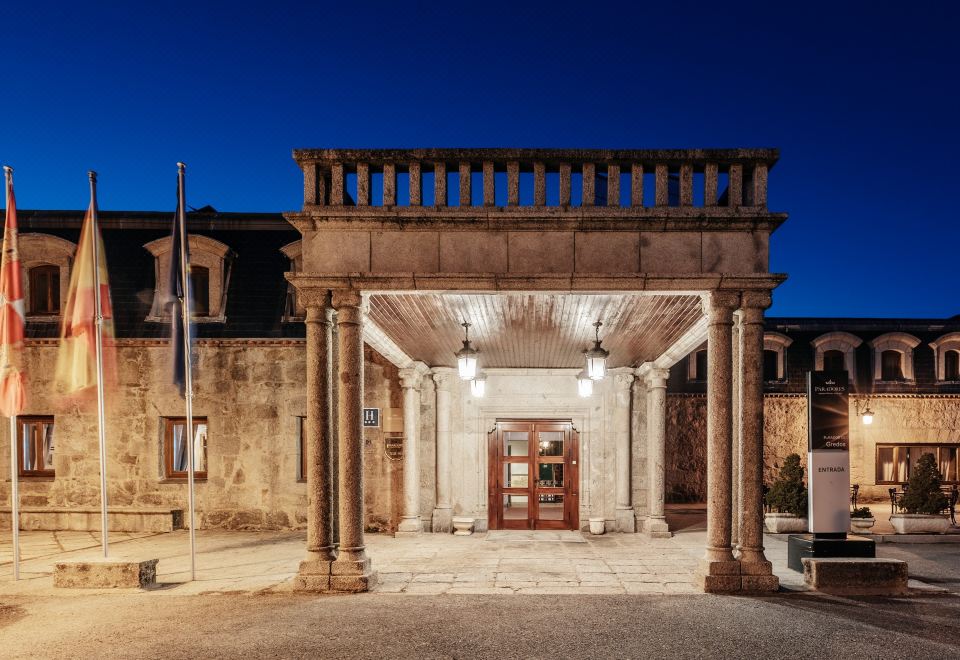 a grand entrance with a stone arch and pillars , leading to a courtyard with a flag , under a blue sky at Parador de Gredos
