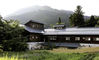 a large wooden house surrounded by lush green grass and trees , with mountains in the background at Ryokan Warabino