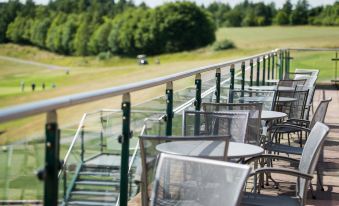 a tennis court is seen through a glass railing , with tables and chairs on a patio at Greetham Valley