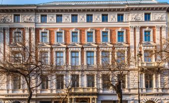 a large , ornate building with multiple windows and balconies , surrounded by trees and clear skies at Hotel Moments Budapest