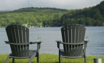 two wooden chairs placed next to each other on a grassy area near a body of water at Lake Bomoseen Lodge