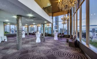 a large , well - lit room with multiple tables and chairs set up for an event , possibly a wedding reception at Mercure Brisbane Spring Hill