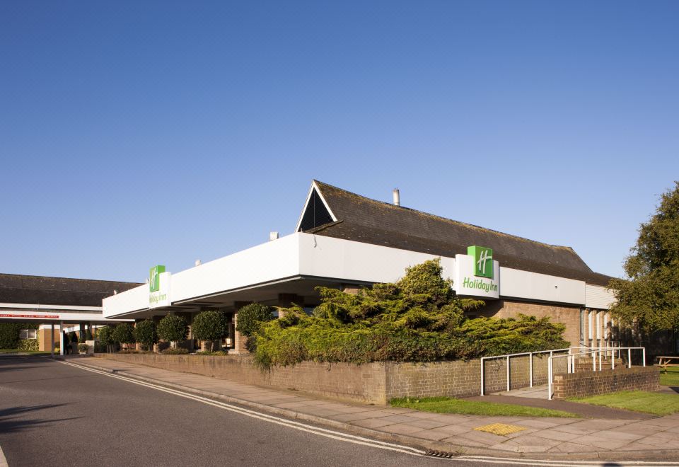 a white building with green and white logos on its roof , situated next to a road at Holiday Inn Ipswich