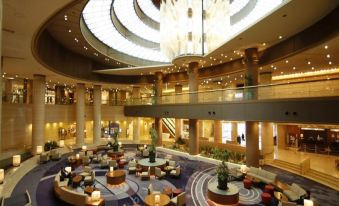 a large hotel lobby with a grand circular chandelier hanging from the ceiling , surrounded by multiple couches and chairs at Kobe Portopia Hotel