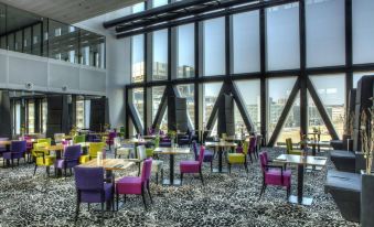 a large room with colorful chairs and tables , a window , and a view of the city at Fletcher Wellness-Hotel Leiden