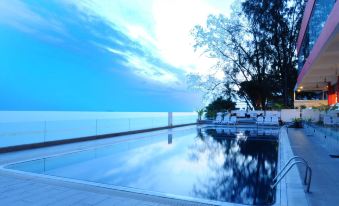 The swimming pool's clear blue water contrasts with the sunny sky in front at Hotel Sentral Seaview @ ​Beachfront
