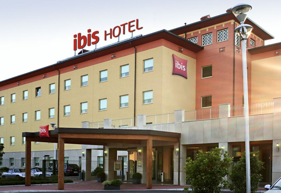 an ibis hotel building with its name displayed on the roof , surrounded by trees and cars parked in front at Ibis Como