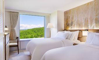 a hotel room with two white beds , one on each side of the room , and a window overlooking a beautiful view at The Westin Rusutsu Resort