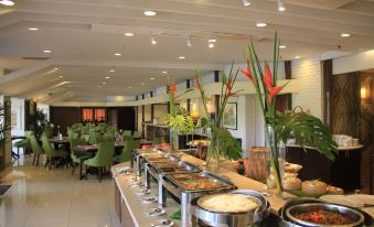 a large buffet table with various food items and flowers in vases , surrounded by green chairs at Impiana Hotel Ipoh