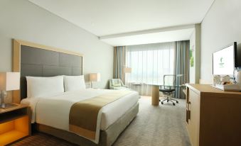 a modern hotel room with a large bed , white bedding , and a desk near the window at Holiday Inn Jakarta Kemayoran, an IHG Hotel