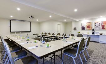 a conference room with a long table , chairs , and a projector screen is set up for a meeting at Ibis Styles Canberra Tall Trees