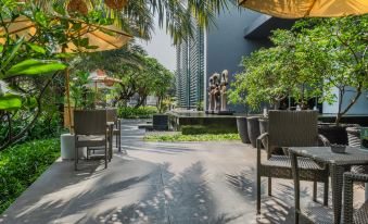 a courtyard with several chairs and tables set up for outdoor dining , surrounded by trees and a tall building in the background at Holiday Inn Jakarta Kemayoran, an IHG Hotel
