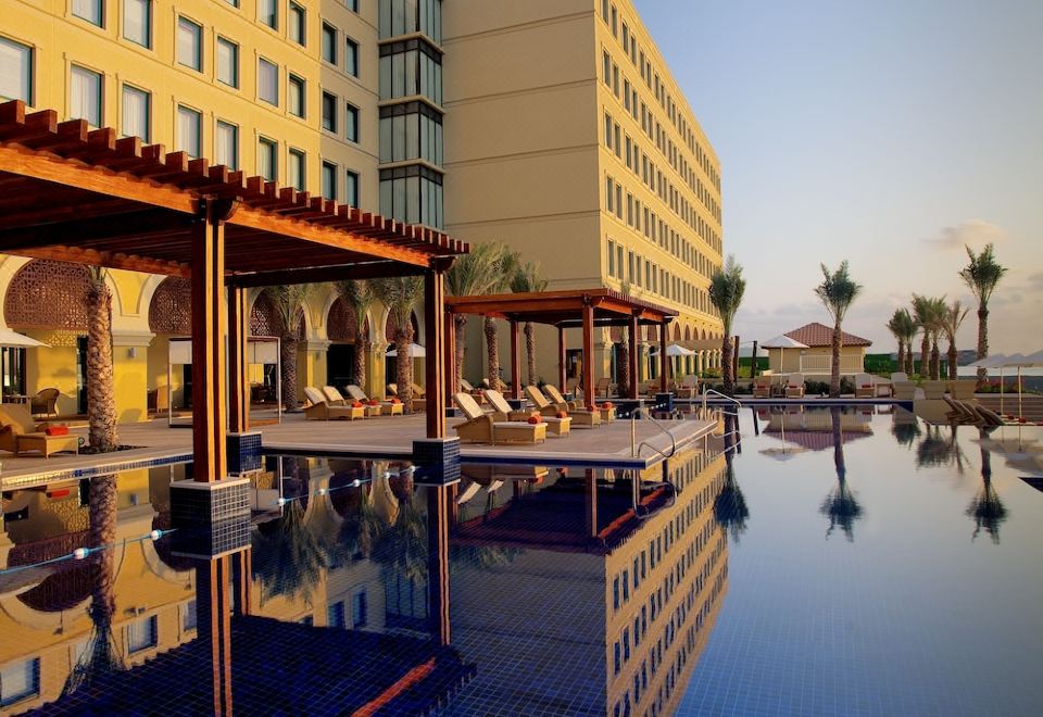 a large swimming pool with several lounge chairs and umbrellas is in front of a modern building at Djibouti Palace Kempinski