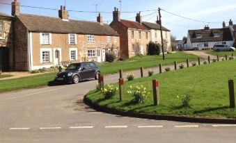 a car is driving on a road next to a row of brick houses with yellow flowers in front at Chalk and Cheese