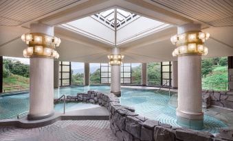 a large indoor pool surrounded by pillars , with several chairs placed around the pool area at Izu Marriott Hotel Shuzenji