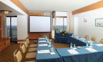 a conference room set up for a meeting , with tables and chairs arranged in a semicircle around a projection screen at Hotel Estoril Eden