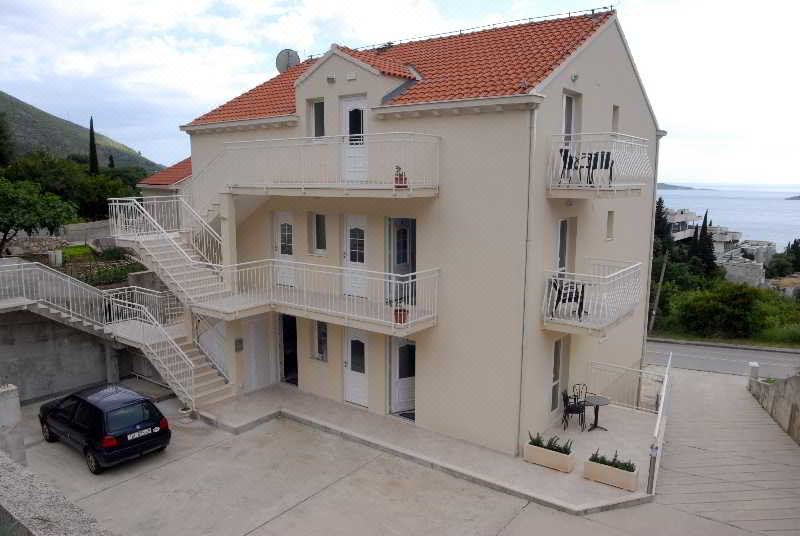 a two - story apartment building with a red tile roof and white balconies , situated in a parking lot at Villa Samba