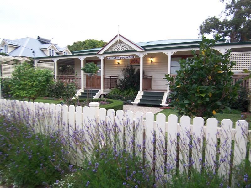 a white picket fence surrounding a lush garden , with a house in the background surrounded by greenery at Reid's Place