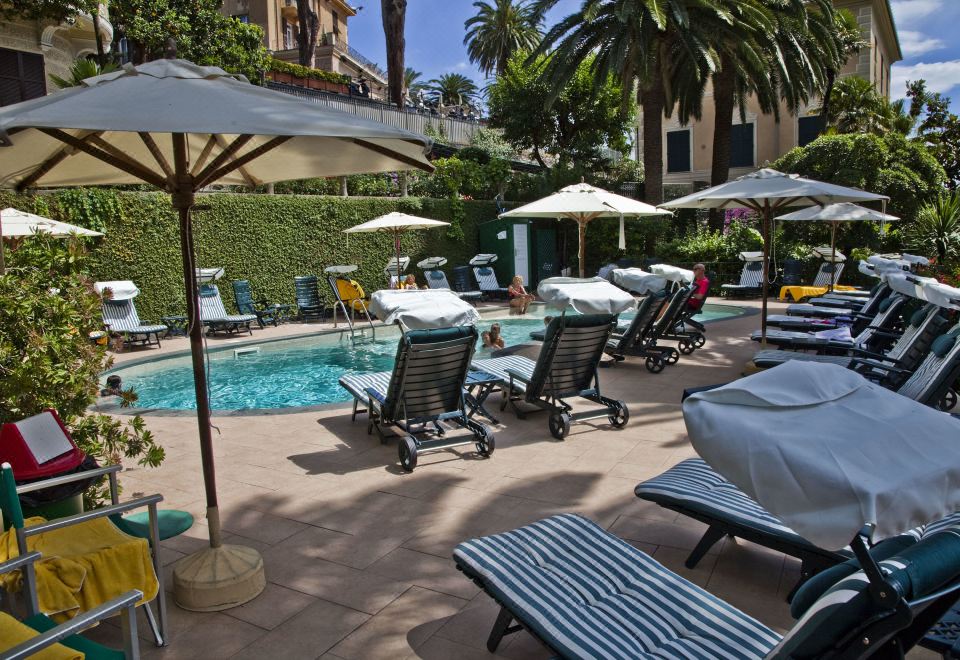a backyard with a swimming pool surrounded by lounge chairs and umbrellas , creating a relaxing atmosphere at Hotel Metropole