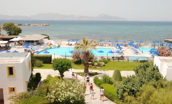 a large swimming pool is surrounded by palm trees and people , with mountains in the background at Mastichari Bay Hotel