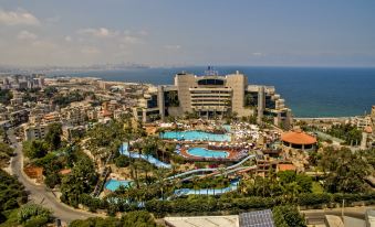 a large resort with a swimming pool surrounded by palm trees and a city in the background at Le Royal Hotel - Beirut