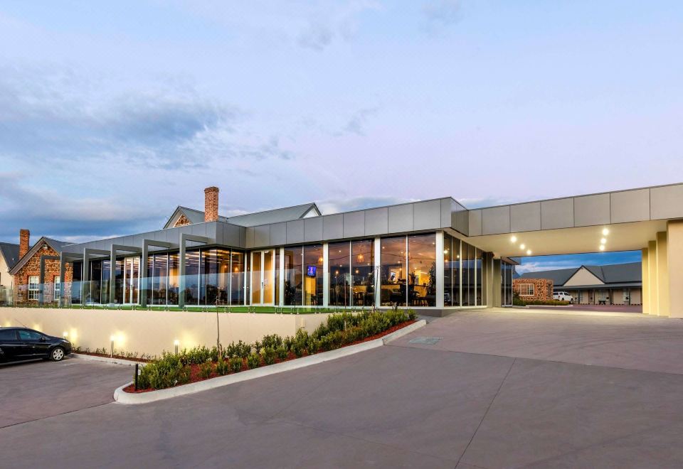 a modern building with a large glass facade and multiple windows is surrounded by greenery at Mercure Goulburn