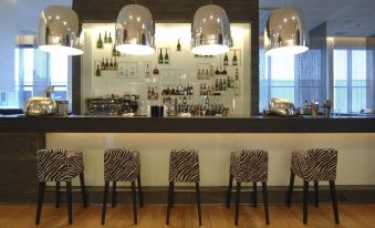 a bar area with several chairs and stools arranged around it , creating a cozy atmosphere at Hilton Helsinki Airport