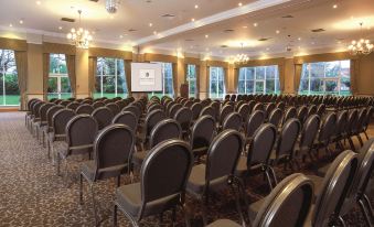 a large conference room with rows of chairs arranged in a semicircle , and a projector screen on the wall at Macdonald Craxton Wood Hotel