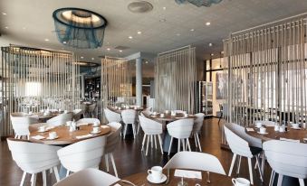 a modern restaurant with white chairs and tables , a bar , and blue curtains on the windows at Scandic Havet