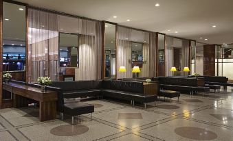 The lobby, featuring large windows and black couches and tables in the center, exudes an elegant ambiance at Hotel Pennsylvania