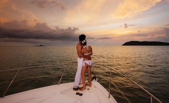 a man and a woman are standing on a boat in the ocean , looking at the sunset at Resorts World Langkawi