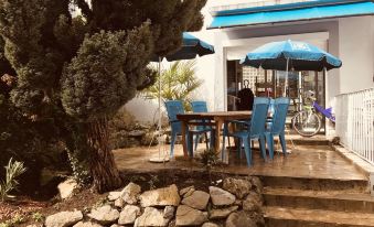 a patio with a blue umbrella , chairs , and an umbrella stand , surrounded by rocks and trees at Myosotis