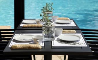 a dining table set with white plates , bowls , cups , and utensils , along with a view of the ocean in the background at Lena Mare Boutique Hotel