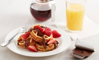 a plate of waffles with strawberries and chocolate syrup is shown next to a glass of orange juice at Residence Inn Gravenhurst Muskoka Wharf