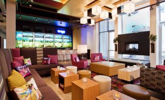 a modern lounge area with various seating options , including couches , chairs , and tables , arranged around a large glass table at Aloft Milwaukee Downtown
