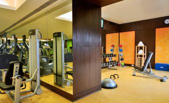 a well - equipped gym with various exercise equipment , including treadmills and weights , under a large window at Courtyard by Marriott Mumbai International Airport