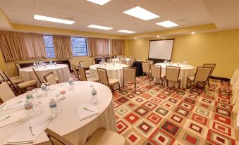 a large conference room with round tables and chairs , water bottles , and a projector screen at Holiday Inn Clinton - Bridgewater