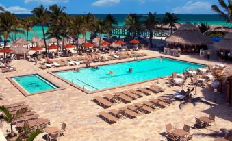 a large swimming pool with a palm tree and lounge chairs , surrounded by palm trees and a beach at Newport Beachside Hotel & Resort
