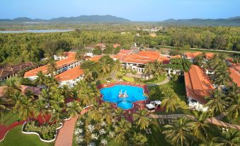 aerial view of a resort with a large pool surrounded by palm trees and buildings , located in the countryside at Holiday Inn Resort Goa