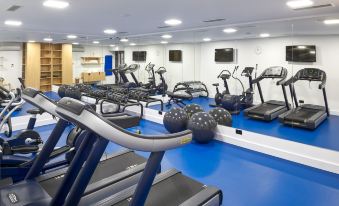 a well - equipped gym with various exercise equipment , including treadmills and stationary bikes , arranged on a blue floor at Sia Split Hotel