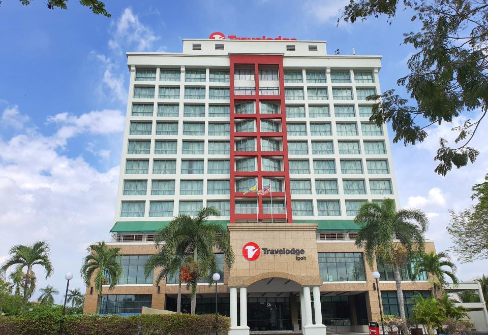a tall building with a red and white facade , surrounded by palm trees and other vegetation at Travelodge Ipoh