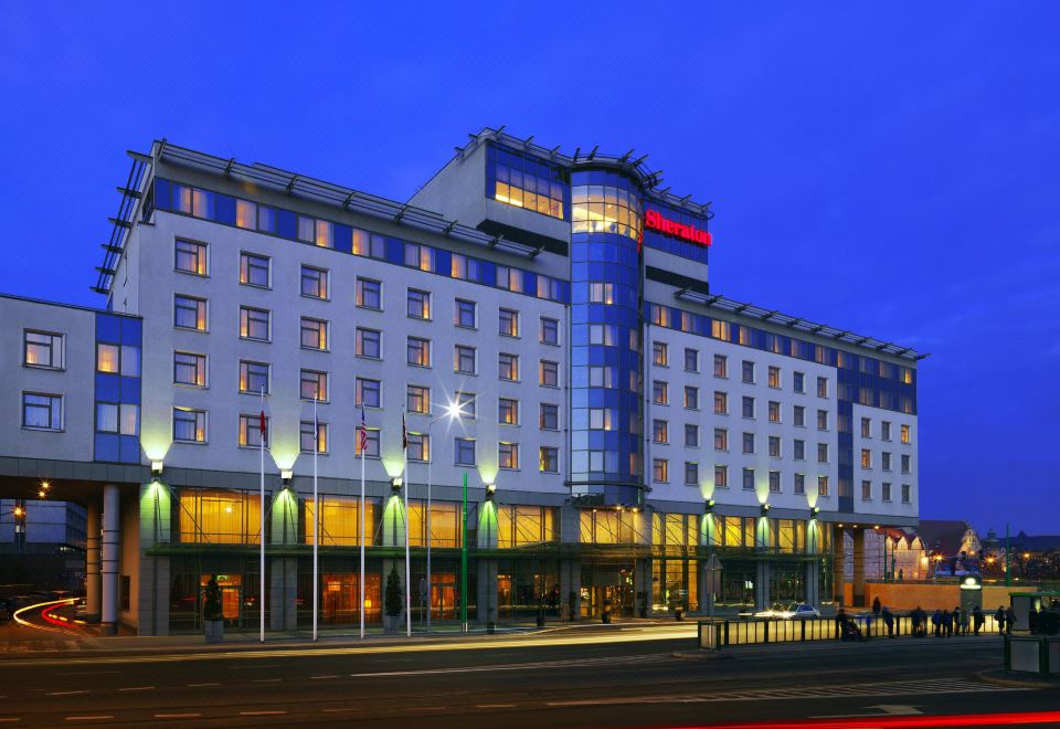 a large hotel building with many windows and a red sign on the front , situated in a city at night at Sheraton Poznan Hotel