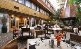 an elegant restaurant with wooden tables and chairs , flowers in vases , and a large window at Forest Park Hotel