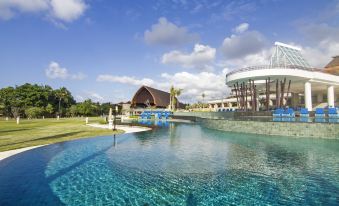 a large swimming pool surrounded by lush greenery and a building in the background at Merusaka Nusa Dua