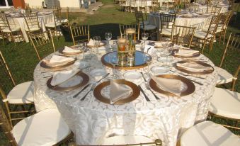 a round table is set with gold and white plates , silverware , and a centerpiece for an outdoor event at Atami Escape Resort