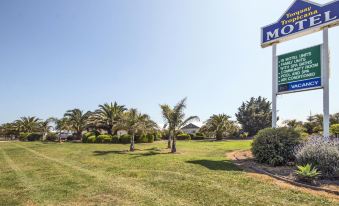 "a grassy field with a sign that reads "" motel "" prominently displayed , surrounded by trees and a blue sky" at Torquay Tropicana Motel